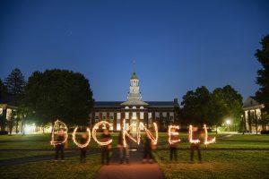 Eight people standing in front of Bertrand Library at dusk using sparklers to spell out "BUCKNELL"